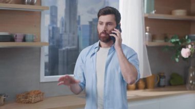 Şık bir genç adam, modern bir mutfak ortamındayken aktif olarak bir telefon görüşmesi yapıyor.