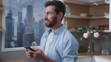 Bir adam akıllı telefonuyla şehir siluetine bakan şık, çağdaş bir mutfakta derinden meşguldür.