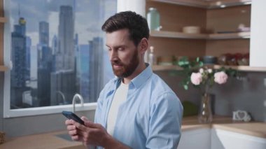 Bir adam şık ve çağdaş bir mutfakta akıllı telefonuyla büyüleyici şehir manzarası sunar.