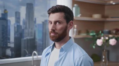 Düşünceli bir adam arkasında çarpıcı bir panoramik şehir silüeti olan şık bir mutfakta özgüvenle duruyor.