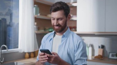 Modern bir mutfak ortamında akıllı telefon kullanan gülümseyen bir adam, bağlantıyı ve teknolojiyi vurguluyor..