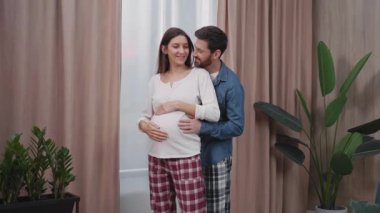 Evlenmiş genç bir adam ve güzel hamile bir kadın oturma odalarında sarılıyorlar. Planlı hamilelik. İlişki. Yetişkin aile hayatı.