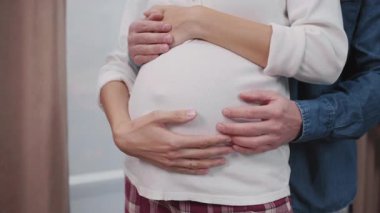 Hamile bir kadınla beyaz bir aile. Mutlu koca karısına sarılıyor ve karnına dokunuyor. Sağlıklı hamilelik. Ebeveynlik.