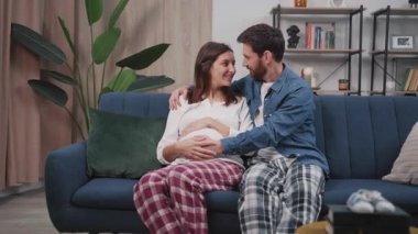 Aile hayatı. Oturma odasında oturan sevgi dolu evli bir çift. Mutlu koca hamile karısına sarılıyor ve onu öpüyor..