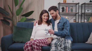 Evli, mutlu koca ve hamile bir eş. Kanepede bebek ayakkabılarıyla oynuyorlar. Planlı hamilelik. Ebeveynler.