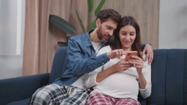 Beyaz tenli, tapılası, hamile karısı olan bir çift akıllı telefon teknolojisi kullanarak internet alışverişini birlikte yapıyorlar. - Aile. İlişki.