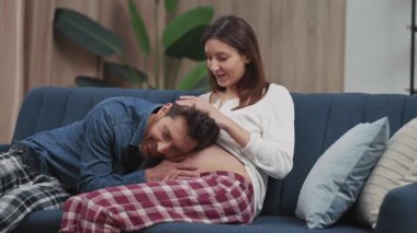 Tatlı, evli, hamile bir çift ve bebek dinleyen kocası kucaklaşan göbeği tekmeliyor. Destek. Hamilelik. Aile kavramı.