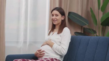 Portreli, genç, beyaz, hamile bir kadın bebeğin karnına nazikçe dokunmasını ve kucaklamasını bekliyor. Planlı hamilelik. Annelik. Duygular.