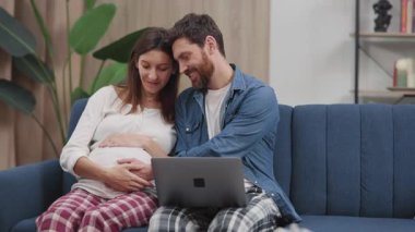 Müstakbel anne babalar bebek göbeğine sarılıp kanepede oturup dizüstü bilgisayarla sohbet ediyorlar. İlişki. Aile hayatı. Ebeveynlik.