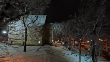 FPV insansız hava aracı akşam şehrine iniyor. Şehir merkezindeki caddelerin ve manzaraların tarihi kar manzarası. Kış şehri manzarası. Gezmeye..