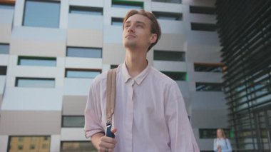 Sırt çantası takan beyaz bir erkek öğrenci güzel yüksek teknolojili kampüs üniversite binasında yürüyor. Çağdaş mimari. Eğitim.