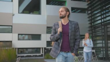 Üniversite kampüsünden çıkarken sırt çantası takan yakışıklı, beyaz bir adam. Yüksek teknoloji mimarisi. Modern gençlik. Öğrenciler.