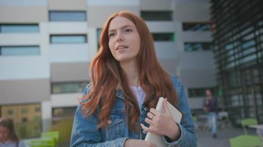 Genç, kızıl, güzel, mutlu, tabletli genç kız üniversite kampüsünün yakınında yürüyor. Modern gençlik. Genç nesil. Teknoloji. Eğitim.