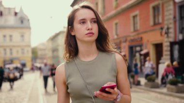 Canlı bir şehir ortamında, genç bir kadın şehrin atmosferinin tadını çıkarırken akıllı telefonuna derinden odaklanır.