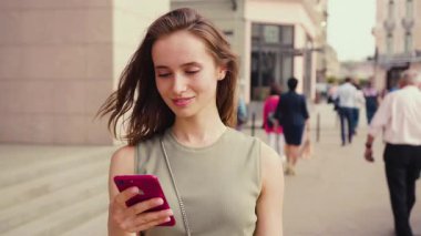 Genç bir kadın, hareketli bir şehir ortamında dolaşırken akıllı telefonunu kullanmaktan zevk alıyor.