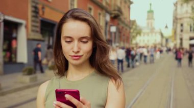 Kalabalık bir şehir sokak sahnesinin ortasında genç bir kadın akıllı telefon cihazıyla mutlu mesut meşgul.