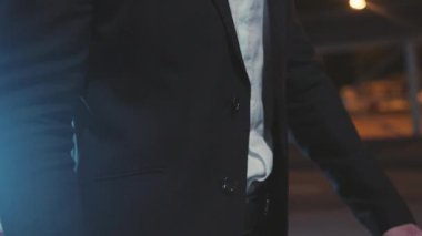 Şık giyinmiş bir adam gece saatlerinde şehir ortamında güven içinde durur.