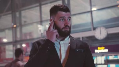 Kendine güvenen bir işadamı, yoğun bir havaalanı ortamında telefon görüşmesi yapıyor.