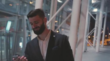 Takım elbiseli profesyonel bir adam modern bir seyahat sergileyen çağdaş bir havaalanı ortamında telefonunu kontrol ediyor..