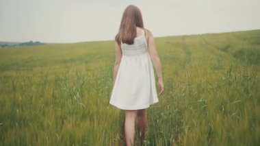 Beyaz elbiseli genç bir kızın yeşil tarlada yürürken görüntüsü. İnanılmaz bir manzara. Doğa, fikir, kavram. Tatillerde. Yaz zamanı..