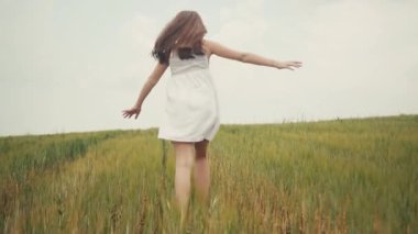 Yeşil tarlada koşan beyaz elbiseli mutlu kızın arka plan görüntüleri. Buğday sapları. Dışarı çıkın. Köy. Keyfin yerinde. Güneşli bir gün. Yaz zamanı.