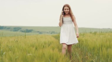 Beyaz elbiseli güzel bir genç elinde akıllı telefonuyla arıyor. Akıllı telefondan konuşan çekici liseli kız. Saha. Şehir dışında. Köy. Yaz zamanı. Açık havada..