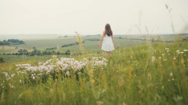 Çiçek açan tarlanın güzelliğinin tadını çıkaran beyaz elbiseli genç bir kızın arka planı. Doğa. Batı Ukrayna. Yaz zamanı. Açık havada. Göz kamaştırıcı manzara.