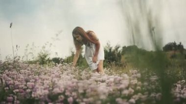 Sahada yürüyen genç bir kızın romantik görüntüsü. Gündüz vakti. Şefkat. Küçük beyaz bir bayan çiçek toplayıp kokluyor. Açık havada..