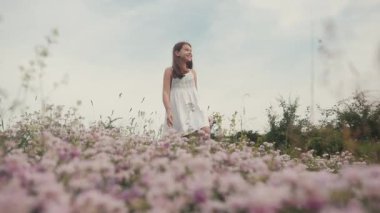 Ön cephede narin pembe çiçekler. Tarlada yürüyen büyüleyici küçük bir kız resmi. Dışarı çıkın. Köy. Yaz zamanı. Güneşli bir gün. Görüntü.