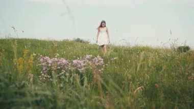 Ahenkli gülümseyen beyaz, romantik elbiseli beyaz kız sahada el kaldırıyor. Bitki, çiçekler. Muhteşem bir manzara. Yaz zamanı. Açık havada. Köy.