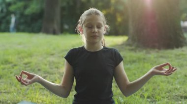 Lotus pozisyonunda oturan güzel bir kız. Genç bir kız kameraya bakıp gülümsüyor. Açık havada. Yaz zamanı. Köy.