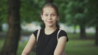 Güzel görünümlü beyaz bir kızın kameraya bakıp gülümsemesini çekmek. Arkadaş canlısı bir yüz. Açık havada. Yaz zamanı. Şu anda, zinde ve sağlıklı, disiplinli, rutin bir kız.