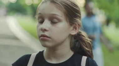 Hayal kırıklığına uğramış, koyu yeşil gözlü kızın yakından çekilmiş portresi kameraya dikkatle bakıyor. Ciddi bir genç kız. Açık havada. Yaz zamanı. Yeşil arkaplan.