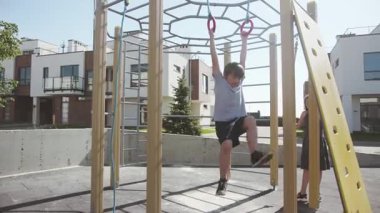 İki mutlu kardeş evlerinin yakınındaki oyun alanında eğleniyorlar. Kız kardeşi gülerken iplere asılmış spor egzersizi yapan sevimli, güçlü, aktif bir çocuk..