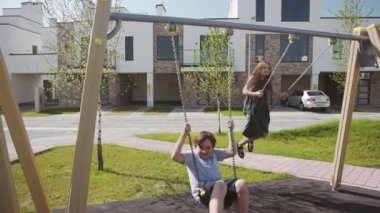 Güneşli yaz havasında salıncakta uçan heyecanlı kardeşler. Evlerinin yakınındaki avluda sallanan iki mutlu çocuk..