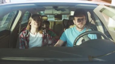 Modern şehirde arabayla gezen neşeli genç bir aile. Ailelerin ve çocukların birlikte seyahat ettiği güzel bir yaz seyahati..