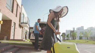 Şirin kız, güneşli caddedeki araba bagajına ağır bir bavul götürüyor. Yakışıklı baba, kızının eşyaları arabaya yüklemesine yardım ediyor. Yazın aile tatili.