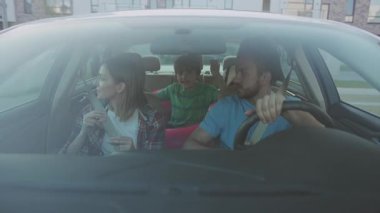 NEW YORK - 5 Nisan 2018: Yeni evlerine gitmek için arabada oturan mutlu genç aile. Heyecanlı aileler ve çocuklar yazın eğlenceli bir yolculuk sırasında müzik eşliğinde dans ediyorlar..