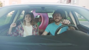 Evli çiftlerin ve şehirde araba süren çocukların ön görüntüsü. Neşeli baba ve çocukları deniz kenarına giderken arabada eğlenirken beşlik çakıyor..