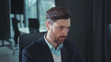 Yorgun genç iş adamı bilgisayar kullanıyor. Modern ofis teknolojisi portresi şirketinin ağır çekimde kapanış yaptığı için baş ağrısı çekiyor.