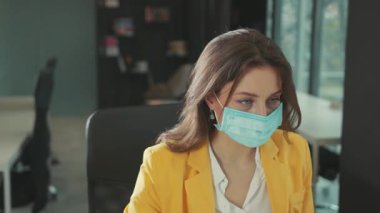 Koruyucu yüz maskesi takan sağlıklı beyaz iş kadını beyaz cerrahi eldivenler ofis bilgisayarında çalışmaya devam eden temiz havayı soluyor..