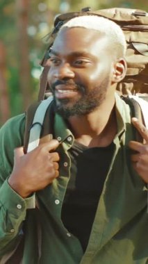 Parlak bir gülümsemesi olan genç bir adam güvenilir sırt çantasıyla açık havada bir maceraya hazır.