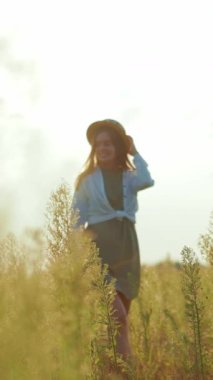 Şık şapkalı bir kadın, uzun bir çim tarlasını keşfeder. Güneşli ve huzurlu bir ortamda özgürlük ve sükunet uyandırır.