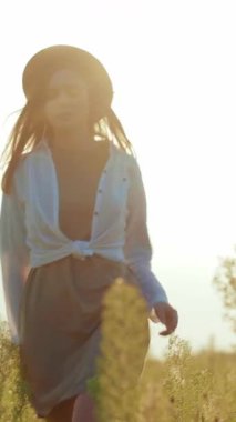 Huzurlu bir videoda, saman şapkalı, yemyeşil bir alanda duran, doğal güzelliği ve kadınlığı kucaklayan bir kadın görülüyor.