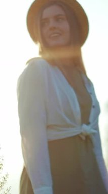 Hasır şapkalı bir kadın güneşli bir tarlada zarif bir şekilde duruyor, elinde bir buket çiçekle günbatımı huzurlu atmosferi güçlendiriyor.