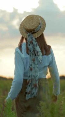 Hasır şapkalı bir kadın dingin bir tarlayı keşfeder, neşe ve huzuru yansıtır, titreyen manzarada yürürken, doğayı kucaklayarak.