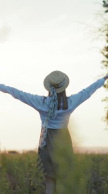 Hasır şapkalı bir kadın güneşli bir tarlada sevinçle duruyor, kollarını açmış, doğa güzelliğini kucaklıyor ve özgürlüğünü kucaklıyor.