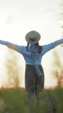 Bu sakin videoda, saman şapkalı ve mavi kazaklı bir kadın bir tarlada duruyor, kollarını açmış güzelliği kucaklıyor, neşe saçıyor.