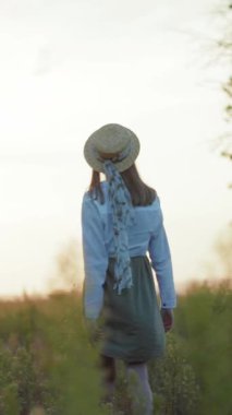 Şık şapkalı bir kadın güneşli bir alanda duruyor, kollarını açmış güzelliği kucaklıyor, güzel bir arka planda neşe ve özgürlük sunuyor.