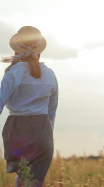 Bu sakin videoda, saman şapkalı bir kadın canlı bir tarlada yürüyor, güneşin tadını çıkarıyor, ve nefes kesici manzaralara hayran olmak için duruyor.